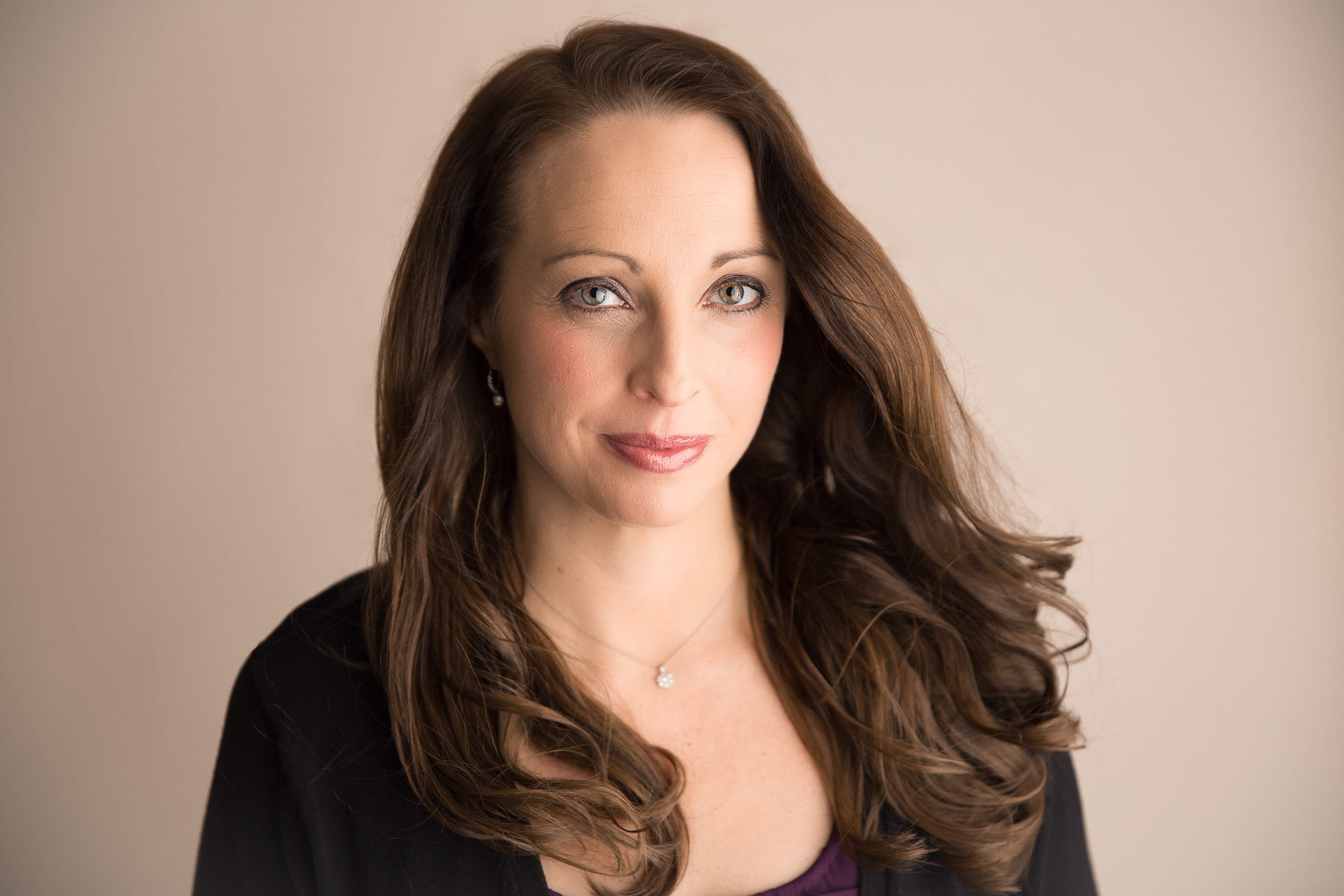 Professional headshot of Jessica Rock, Esq., a woman with long brown hair, light eyes, and a confident smile, wearing a dark top and necklace, against a neutral background.