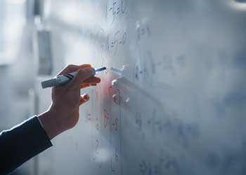 Close-up of a student writing mathematical equations and calculations on a whiteboard during a classroom lesson. The image highlights problem-solving, critical thinking, and analytical skills developed through advanced study in mathematics and quantitative reasoning.