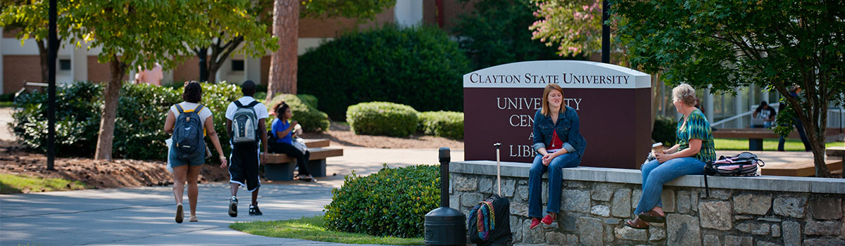 picture of two people sitting on a brick wall and several people walking by the university center