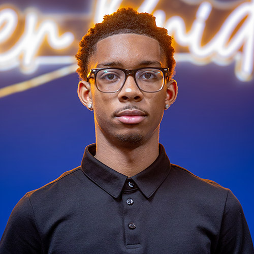 Image of Mykell Strickland wearing a black polo-sytle shirt and black horn-rimmed glasses