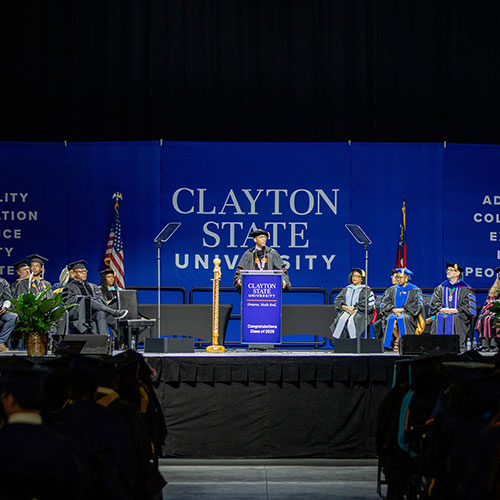 president lewis speaking behind a podium with others on the stage at commencement